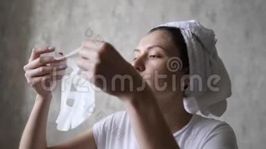 化妆品天然面膜抗老化和面部皱纹。 一个年轻的女人用毛巾敷面膜来滋润脸部